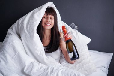 Kendine ayıracak vaktin var. Kutlama evde. Mutlu genç bir kadın battaniyenin altında oturmuş şampanya içiyor..
