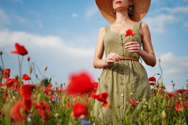 Yaz zamanı. Kırmızı haşhaş tarlasında şapkalı genç bir kadın..