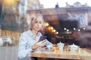 Kablosuz kafe. Genç ve güzel bir kadın kahve içerken akıllı telefon kullanıyor..