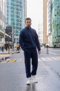 Uzun boylu genç bir adam klasik bir spor takım elbise giyer ve kameraya poz verir. Atletik yakışıklı genç adam kentsel konumda duruyor ve spor takımını gösteriyor. Model
