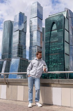 Sakallı, gri kapüşonlu yakışıklı bir hippi portresi ya da logo ya da tasarım için geniş bir kazak. Elinde kahve tutuyordu. Yazdırma için model