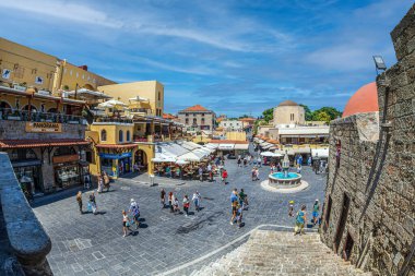 RHODES, GREECE - 30 Haziran 2022: Ortaçağ kentinde, Sokrates, Pisagor ve Aristo caddelerinin kesiştiği noktada, Türk çeşmesi ve 1597 yılından kalma Tüccar Lonja ile birlikte Hipokrat Meydanı.