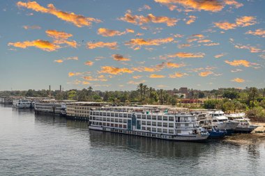 LUXOR, EGYPT - APRIL 24, 2022: Tourist cruise ships on the Nile river, anchored in the tourist port. Sunset light.