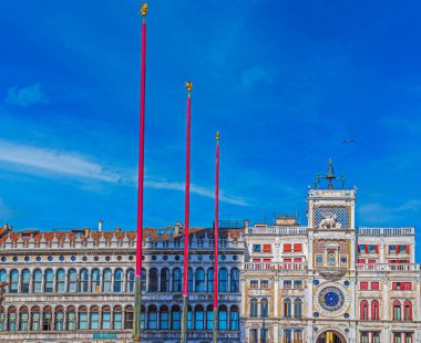 VENICE, İtalya - 16 Mart 2023: kırmızı bayrak direkleri ile San Marco Meydanı 'nda bulunan Torre dell' Orologio manzarası. 1499 'dan Rönesans Kulesi şehir manzaralı ve mekanik saati sembolik dekorasyonlu.