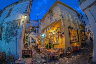 Skiatos Kasabası, Skiatos Adası, GREECE - 22 AĞUSTOS 2023: Eski şehrin Yunan Akdeniz mimarisinde geleneksel tavernalarla dolu dar sokakların akşam manzarası.