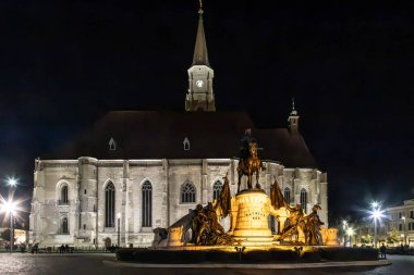 CLUJ-NAPOCA, TRANSYLVANIA, ROMANIA - 6 Ekim 2023: Union Square 'deki St. Michael Kilisesi önündeki Mathias Corvinus Anıtı' nın gece manzarası. 