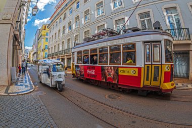 LISBON, PORTUGAL - 8 Nisan 2024: Tuk Tuk adlı komik elektrikli arabalı turistik ulaşım ve şehrin sokaklarında klasik tramvay.