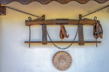 Traditional objects from the old Romanian peasant household as: wooden yoke for oxen, leather shoes called opinci, clay wheel and metal chains, used as external decorative objects on a wall of a house clipart