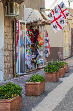 ALGHERO, İtalya - 4 Temmuz 2024: Tipik Sardunya, küçük geleneksel hediyelik eşya dükkanı olan ortaçağ resim caddesi. Sardunya vilayetinin bayrağı cephede sergilendi.