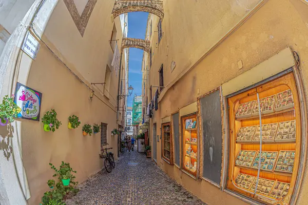 stock image ALGHERO, SARDINIA, ITALY-JULY 4, 2024: View along the medieval and commercial street Carrero de L'arsenal-Vicolo Serra,with small traditional shops,restaurants and specific funny Italian way of life.