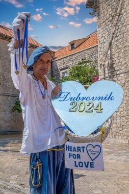 DUBROVNIK, CROATIA - AUGUST 17, 2024: Man dressed in medieval clothes, with the symbol of love, on the main street of the old town, Stradun, in front of Large Onofrio's Fountain. clipart