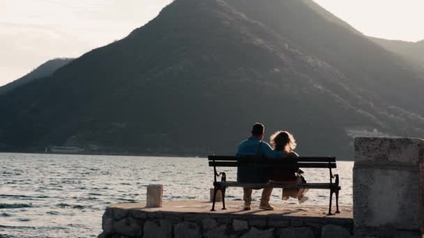 モンテネグロの海に沈む夕日のベンチに座っている2人の若者 高品質のフルHd映像 — ストック動画