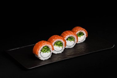 Lezzetli somonlu suşi dürümleri zarif, koyu bir tabakta sunulur. Her yerdeki yemek severleri ayırt etmek için mükemmeldir.