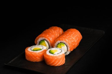 Lezzetli somonlu suşi dürümleri zarif, koyu bir tabakta sunulur. Her yerdeki yemek severleri ayırt etmek için mükemmeldir.