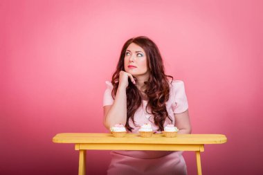 Parlak makyajlı, iri yarı kızıl saçlı bir kadın ve el yapımı tatlı bir çörek. Stüdyo rengi arka plan, alışılmadık duygular. Vücut pozitif, kilo kaybı