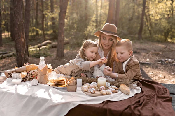 Çocuklu aile bahar bahçesinde Paskalya pikniğinin tadını çıkarıyor. Anne ve çocuklar mutlu bir şekilde yumurta kırıyor, ekmek yiyor, krep yiyor ve kırsal tarzda süt içiyor.