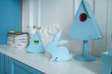 Mavi mutfak içi mobilyalarla dolu. Vazoda çiçekli şık bir mutfak. Bahar dekorunda ahşap mutfak. Sıcak ev dekorasyonu. Mutfak gereçleri, tabaklar masanın üstünde. Mutfak adası yemek odasında, tavşan heykelciği. Paskalya konsepti