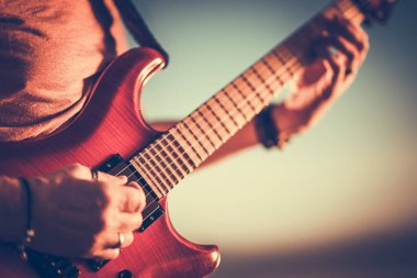 Güneşli bir günde elektro gitar çalan gitaristin yakın çekimi. Bulanık arka plan. Müzik ve Eğlence Teması.
