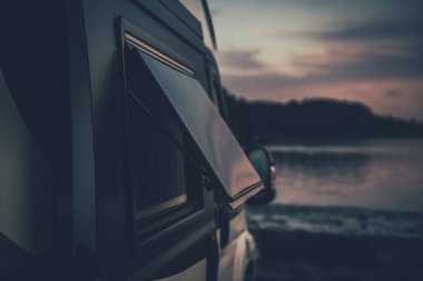 Camper Van 'daki Eğik Pencere' nin Kapanışı Gece Stopover İçin Kıyıya Park Edildi. Arka planda Manzaralı Akşam Manzarası. Motorhome Seyahat Teması.