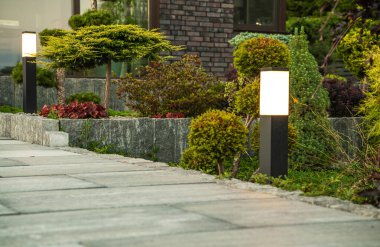 Outdoor Lights, Residential House Backyard 'a Beton Bahçesi Yolu Boyunca Kuruldu. Arka planda peyzajlı çiçek yatakları. Yard Aydınlatma TemasıName.