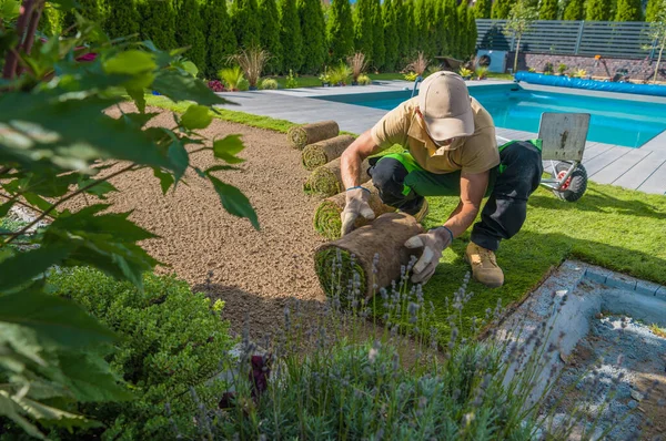 屋外スイミングプールの周りにインスタント芝生をインストールしながら コーカサスの専門庭師は慎重に芝のロールを展開します 裏庭休憩所 — ストック写真
