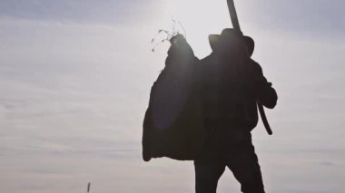 Kovboy Çiftçi elinde ot torbası ve bahçe çatalıyla tarlasında yürüyor.