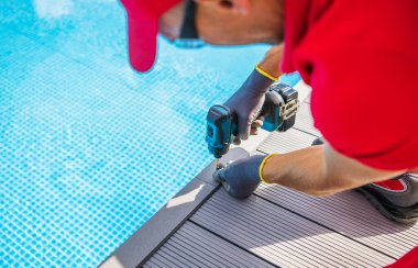 Poolside Composite Deck Building by Professional Worker. Modern Swimming Pool Surrounding. Using Cordless Drill Driver. clipart