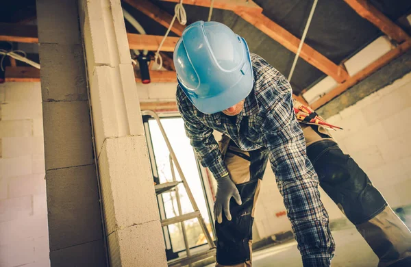 专业建筑工人在蓝色硬帽弯腰为他的工具 背景下的住宅楼宇地盘 — 图库照片