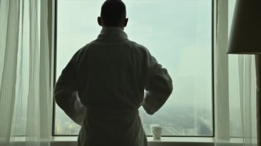 Adam iş seyahatinde yeni bir güne hazırlanıyor. Otel odasının penceresinden bakıyor ve kahve içiyor.