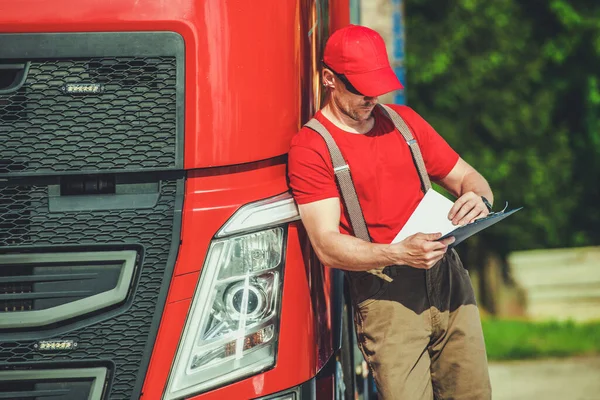 Professional Caucasian Trucker Reviewing Cargo Shipping Documents Before Starting the Road. Transportation Industry Theme.