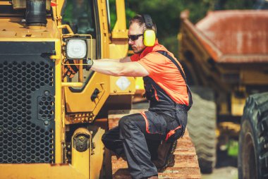 Professional Caucasian Mechanic Inspecting Heavy Duty Industrial Bulldozer at Building Site. Construction Equipment Theme.