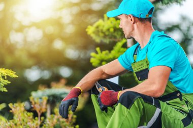 Caucasian Landscaper with Pruning Shears in His Hand Taking a Break During Garden Landscape Maintenance Work.