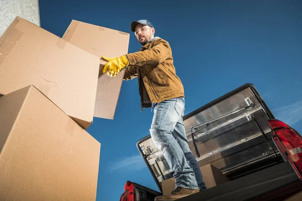 Moving Company Worker Loading Big Cardboard Boxes on the Cargo Bed of His Pickup Truck. Relocation Services Theme.
