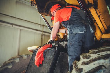 Caucasian Heavy Machinery Mechanic Performing Tractor Maintenance. 