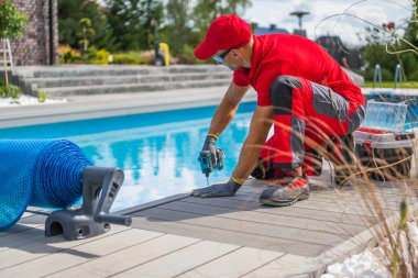 Residential Backyard Swimming Pool Deck Building. Poolside Deck Made From a Modern Composite Panels. Caucasian Worker in His 40s.