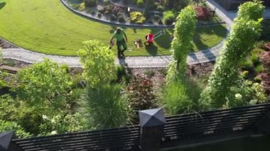Caucasian Men in His 40s with Modern Electric Cordless Leaf Blower Cleaning His Backyard Garden. Aerial View.