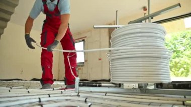 Professional Caucasian HVAC Worker Rolling Over Radiant Floor Heating Plastic Pipeline.