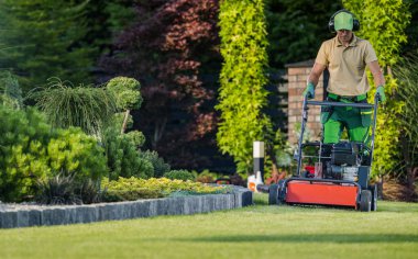 Professional Caucasian Gardener Mowing the Lawn During Backyard Garden Maintenance Work. Gardening Services and Equipment.