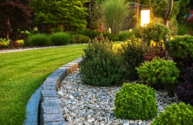 Closeup of Professionally Landscaped Flower Bed with Decorative Green Garden Plants and Evenly Mowed Lawn in the Background.