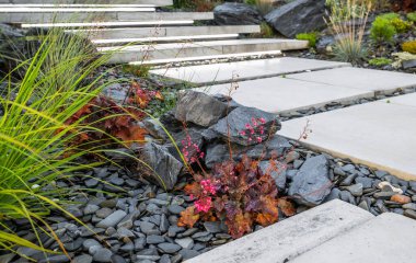 Closeup of Dark Grey Decorative Garden Stones and Pebbles Along the Concrete Slab Pathway. Residential Garden Design Ideas.