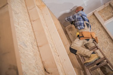Professional Contractor Standing on Ladder During Ceiling Installation in Newly Built Residential House. Construction Theme.
