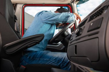 Side View of Tired Truck Driver Sleeping on Steering Wheel Inside Vehicle Cabin After Completing the Route. Truckers Life Theme.