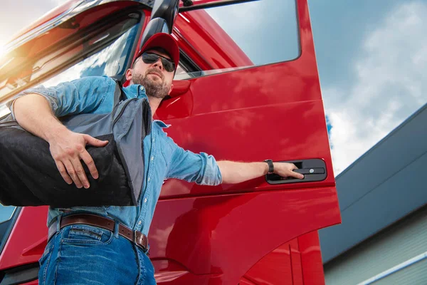 Professional Truck Driver with Travel Bag on His Shoulder Opening the Door of His Heavy Duty Vehicle Cabin Ready to Hit the Road.