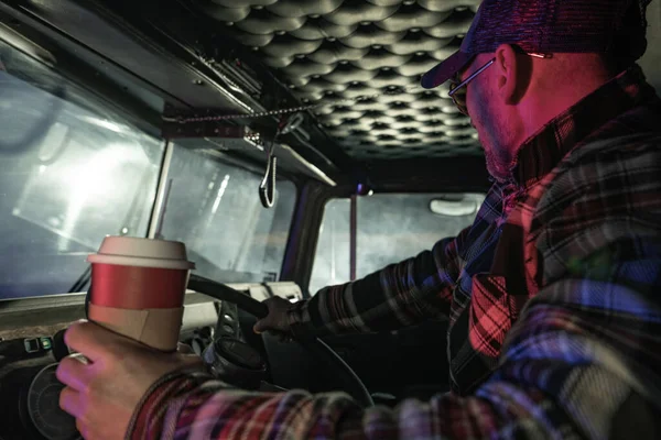 Night Time Semi Truck Driving. Caucasian Trucker Driving and Drinking Fresh Hot Coffee To Get Some Caffeine Boost.