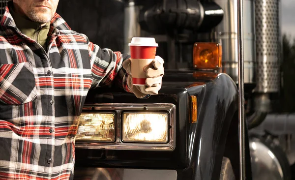Truck Stop Coffee Break. Caucasian Trucker Drinking Hot Drink in Front of His Semi Truck Tractor. Transportation Industry Theme