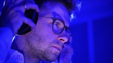 Caucasian Music Producer in His 30s Listening a Music Using Professional Headphones. Entertainment Industry. Dark Blue Illuminated Room.