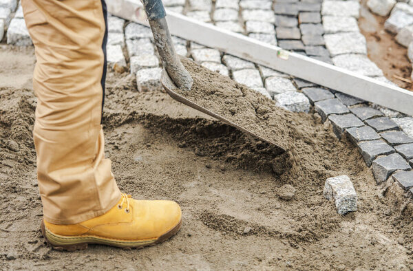 Closeup of Professional Contractor with a Shovel Preparing the Ground for Laying Pavers by Creating Sand Bed. Industrial Theme.