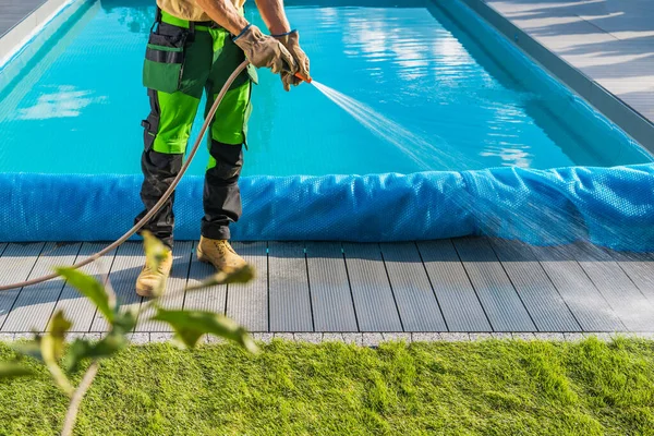裏庭のプールサイドの周りの世話をする ガーデンオーナーウォーターホースを使ったスイミングプールデッキの清掃 — ストック写真