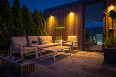 Modern Residential Backyard 'daki Lounge and Dining Area Açık Işıklar, Bitkiler, Bahçe Masası ve Sandalyelerle süslenmiş. Sıcak Yaz Gecesi.