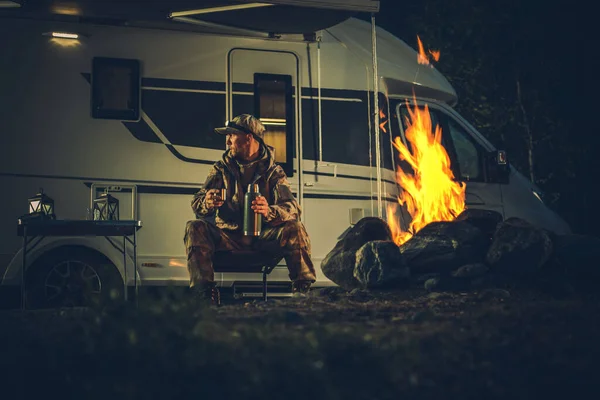 迷彩塗装を身に着けているハンターバーニングキャンプファイヤー彼のモーターホームキャンパーヴァンレクリエーション車両の横にあります 狩猟シーズンのテーマ — ストック写真